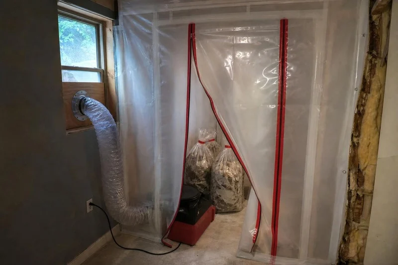 Bagged mold debris going out through a zippered containment exit with the negative air unit still running