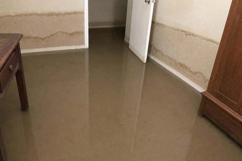 Storm water sits across a Holladay lower-level floor, a dark wet line marking the drywall well above it