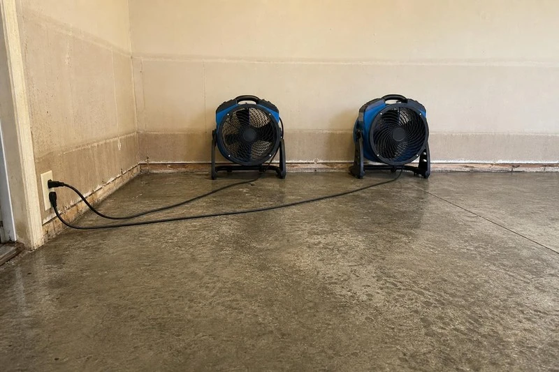 Facing the brown mark on the drywall, two blue movers push air over the dried slab