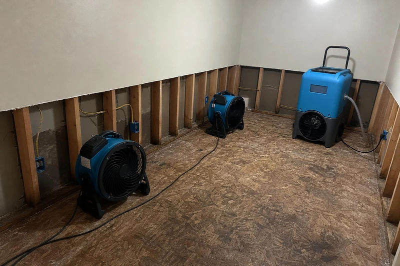An LGR dehumidifier works the far corner of a stripped South Salt Lake room while two movers face the open cavities