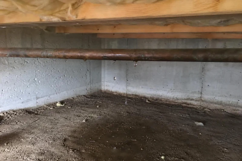 Braided steel supply line burst open along its seam under a floor joist, water falling in a steady stream onto a Salt Lake City basement slab